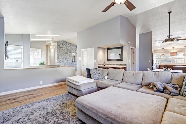 living room featuring hardwood / wood-style flooring, high vaulted ceiling, a skylight, and ceiling fan