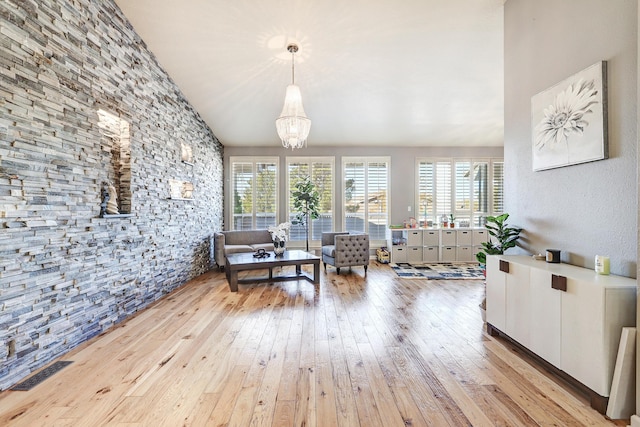 living room with an inviting chandelier, light hardwood / wood-style flooring, a wealth of natural light, and lofted ceiling