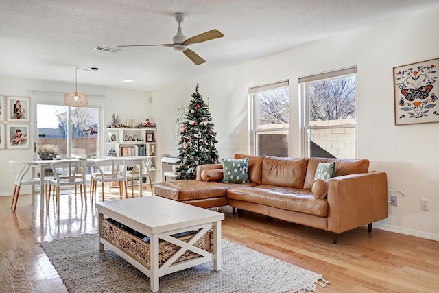 living room with ceiling fan, plenty of natural light, a textured ceiling, and light wood-type flooring