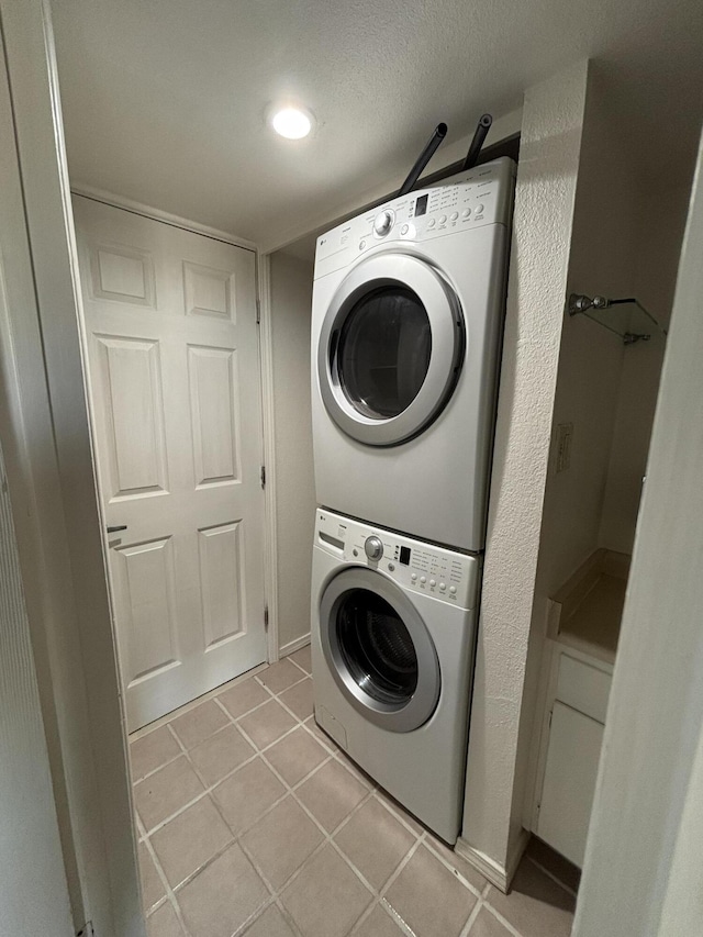 laundry room with stacked washer / dryer, light tile patterned floors, and a textured ceiling