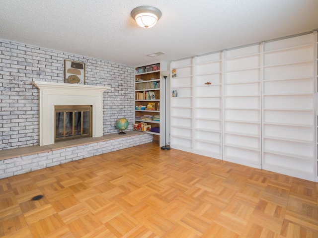 unfurnished living room featuring a fireplace, light parquet flooring, brick wall, and a textured ceiling