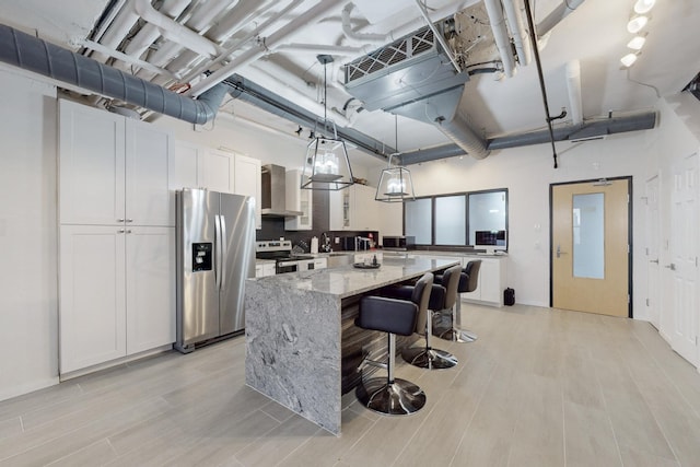 kitchen with white cabinets, light stone countertops, appliances with stainless steel finishes, decorative light fixtures, and a kitchen island