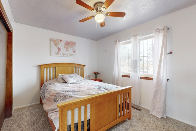 bedroom with ceiling fan, light colored carpet, and a textured ceiling