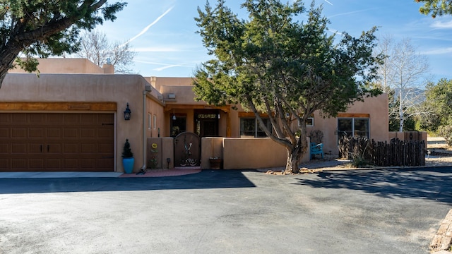 2 Chaco Ct, Sandia Park, NM 87047 - pueblo-style house featuring a gate, an attached garage, stucco siding, and driveway