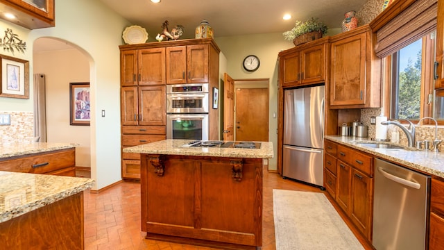 kitchen with light stone countertops, sink, stainless steel appliances, tasteful backsplash, and a kitchen island