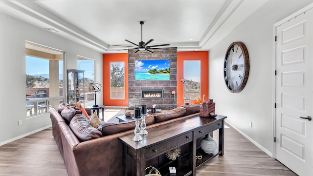 living area with light wood finished floors, a tiled fireplace, a raised ceiling, and baseboards