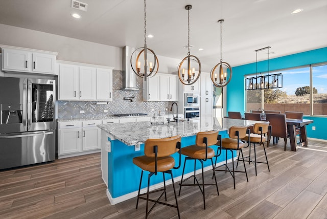 kitchen featuring a kitchen island with sink, stainless steel appliances, visible vents, white cabinetry, and decorative light fixtures