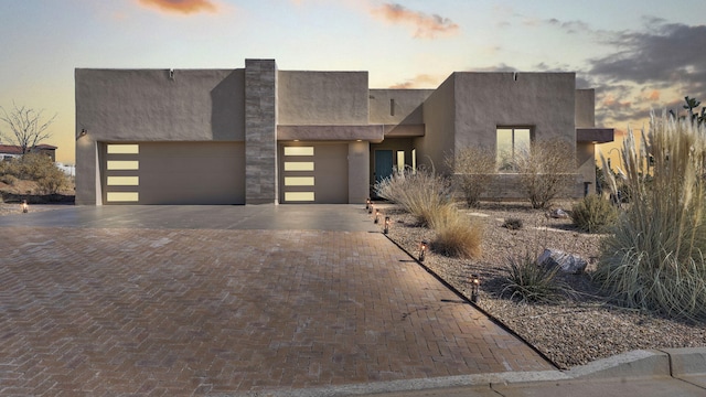 view of front facade featuring a garage, decorative driveway, and stucco siding