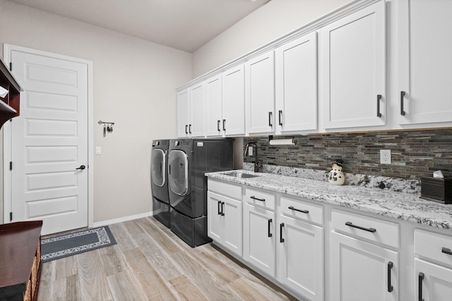 clothes washing area featuring cabinet space, baseboards, light wood-style floors, separate washer and dryer, and a sink