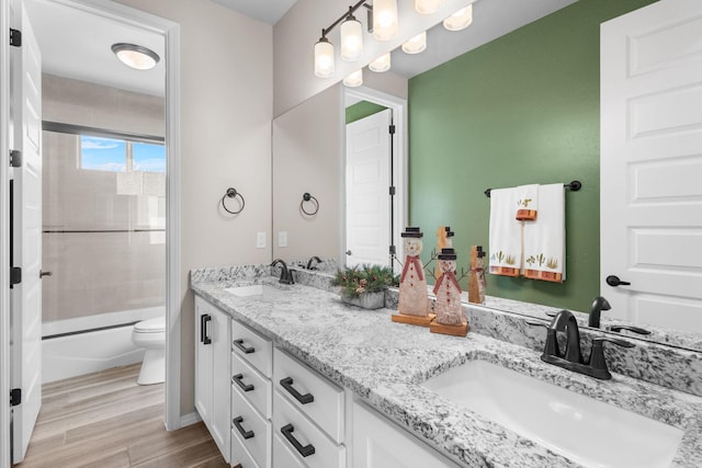 bathroom featuring double vanity, wood finished floors, shower / bath combination with glass door, and a sink