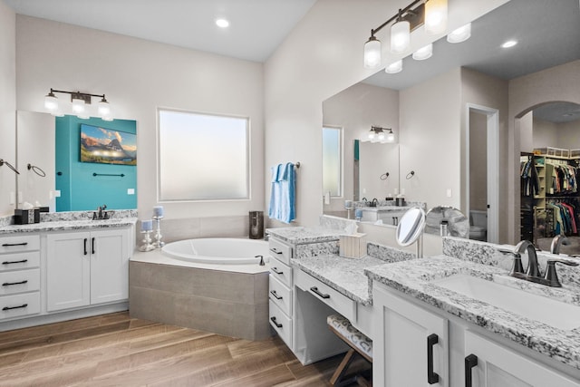 full bathroom featuring two vanities, toilet, a sink, wood finished floors, and a bath