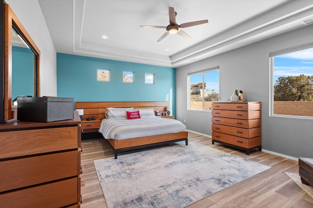 bedroom featuring light wood-type flooring, baseboards, a raised ceiling, and recessed lighting