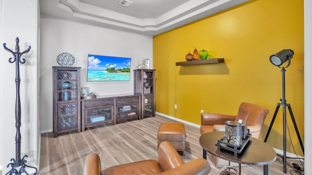 living room featuring a tray ceiling, wood finished floors, visible vents, and baseboards