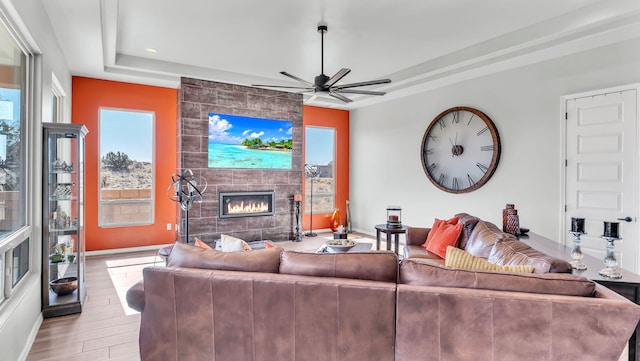 living room featuring baseboards, a ceiling fan, light wood-style flooring, a tray ceiling, and a fireplace