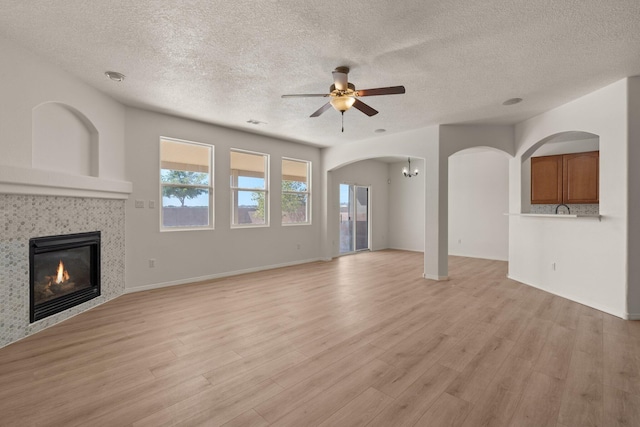 unfurnished living room featuring ceiling fan, a tiled fireplace, a textured ceiling, and light wood-type flooring