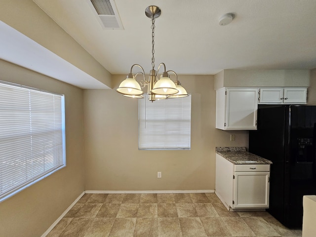 kitchen with dark stone counters, an inviting chandelier, black fridge, hanging light fixtures, and white cabinetry