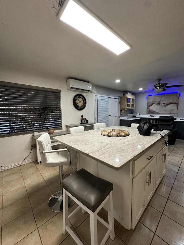 kitchen featuring a wall mounted air conditioner, a breakfast bar, ceiling fan, a kitchen island, and white cabinetry