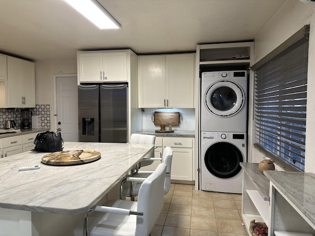 clothes washing area featuring light tile patterned floors and stacked washer and clothes dryer