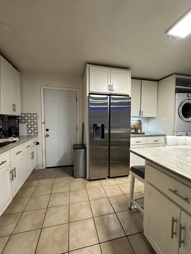 kitchen featuring white cabinetry, stainless steel fridge, stacked washer and dryer, decorative backsplash, and light tile patterned flooring