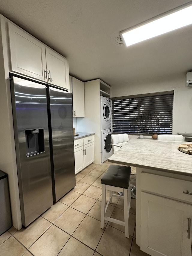 kitchen featuring a kitchen breakfast bar, stainless steel fridge with ice dispenser, light tile patterned floors, white cabinetry, and stacked washer / dryer