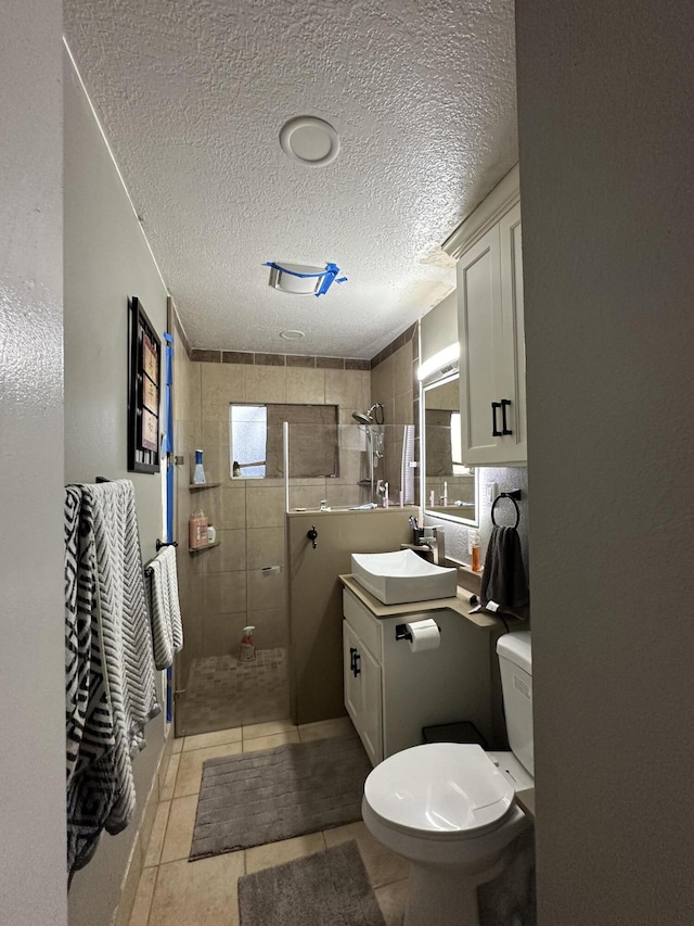 bathroom featuring tile patterned flooring, vanity, a tile shower, and a textured ceiling