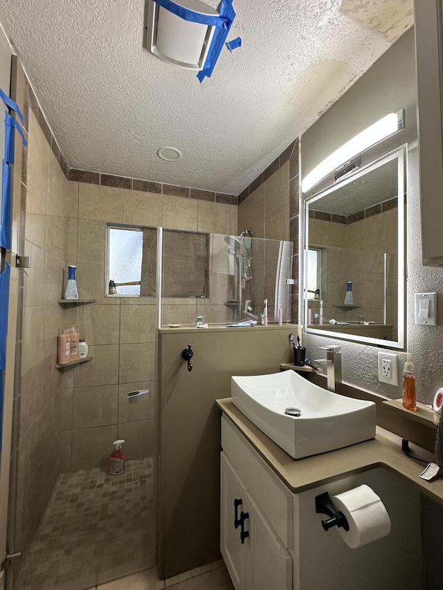 bathroom with a textured ceiling, vanity, and tiled shower