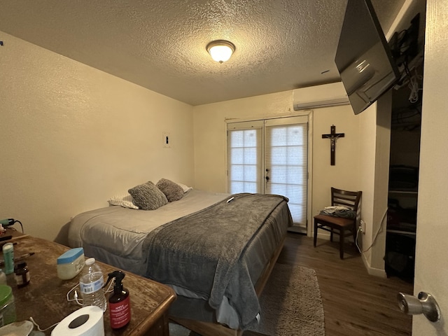 bedroom with a wall unit AC, a textured ceiling, and dark hardwood / wood-style floors