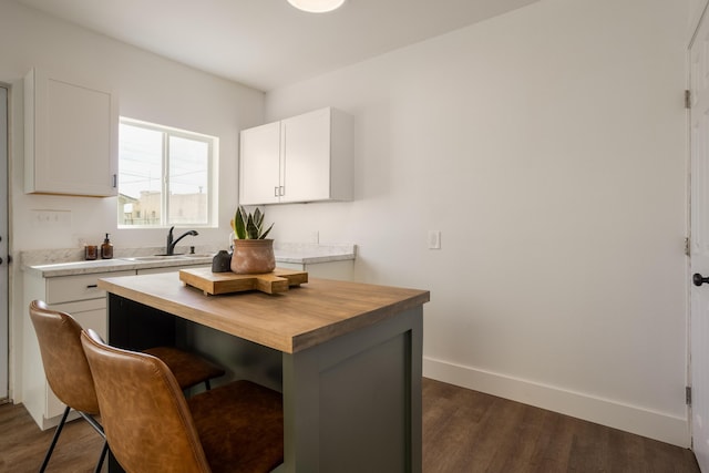 kitchen featuring butcher block counters, sink, dark hardwood / wood-style floors, a breakfast bar, and white cabinets