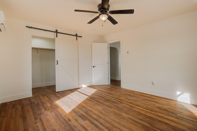 unfurnished bedroom with a barn door, ceiling fan, a closet, and dark wood-type flooring