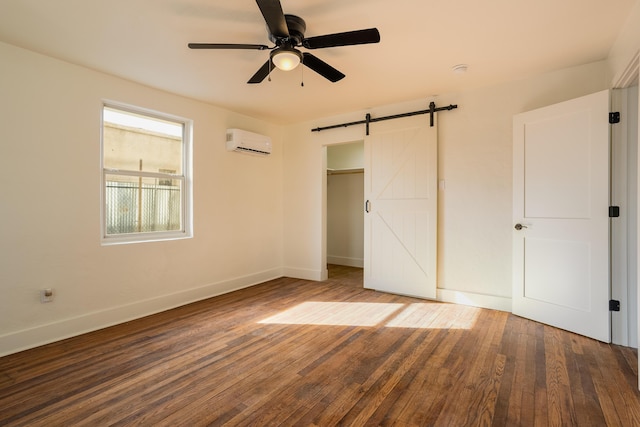 unfurnished bedroom with an AC wall unit, hardwood / wood-style flooring, ceiling fan, a barn door, and a closet