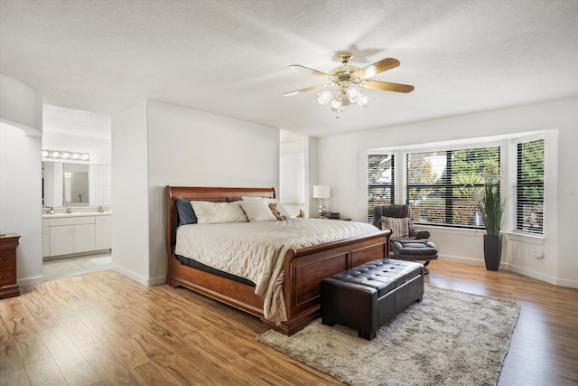 bedroom featuring light wood-type flooring, ensuite bathroom, a textured ceiling, ceiling fan, and sink