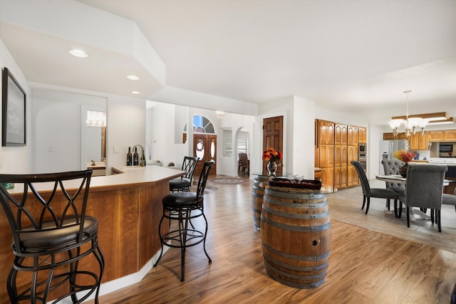 bar with light wood-type flooring, hanging light fixtures, appliances with stainless steel finishes, and a chandelier