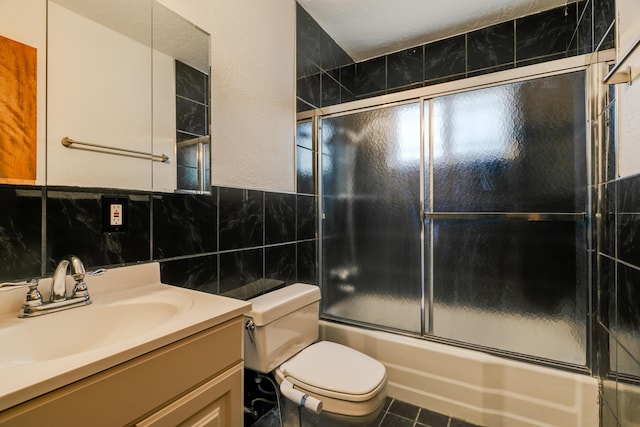 full bathroom with a textured ceiling, toilet, shower / bath combination with glass door, vanity, and tile walls