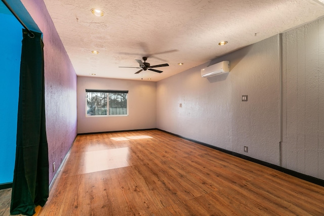 unfurnished room featuring a wall mounted AC, ceiling fan, wood-type flooring, and a textured ceiling