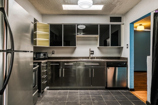 kitchen with dark wood-type flooring, sink, a skylight, a textured ceiling, and appliances with stainless steel finishes