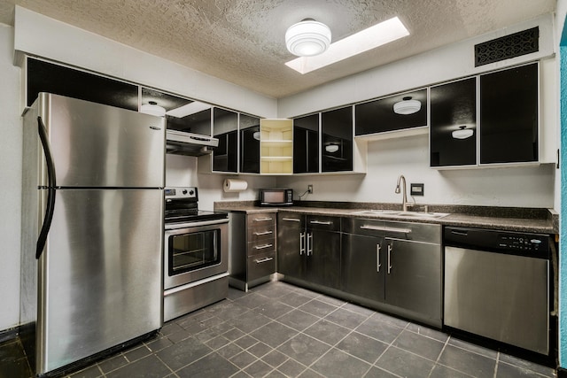 kitchen with sink, range hood, a textured ceiling, dark tile patterned flooring, and appliances with stainless steel finishes