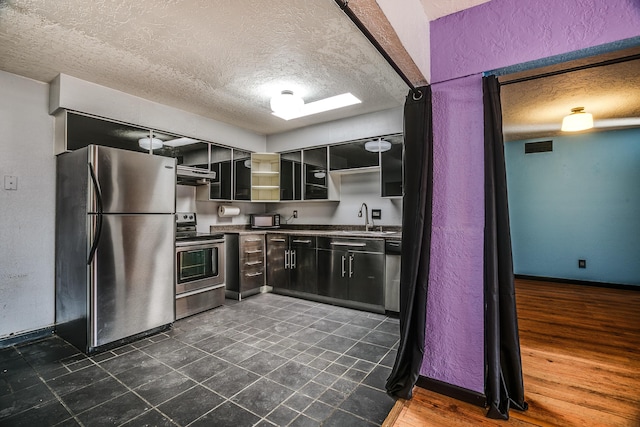 kitchen with sink, dark wood-type flooring, stainless steel appliances, ventilation hood, and a textured ceiling