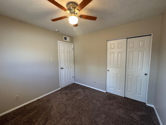 unfurnished bedroom with dark colored carpet, ceiling fan, a textured ceiling, and a closet