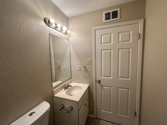 bathroom featuring tile patterned flooring, vanity, toilet, and a textured ceiling