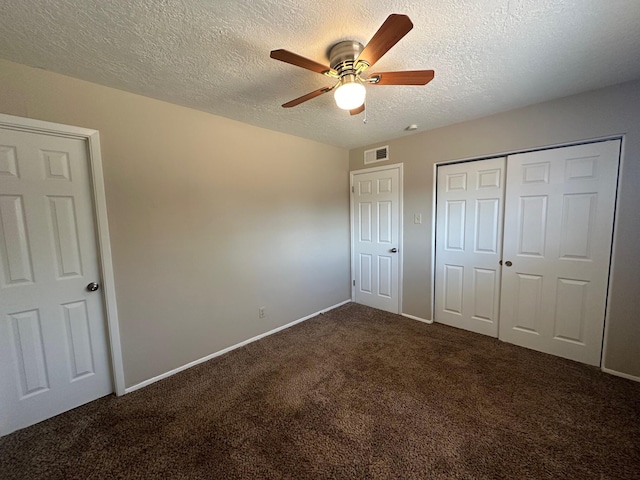 unfurnished bedroom with ceiling fan, a closet, a textured ceiling, and dark colored carpet