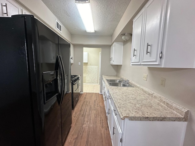 kitchen with a textured ceiling, sink, black appliances, hardwood / wood-style floors, and white cabinetry