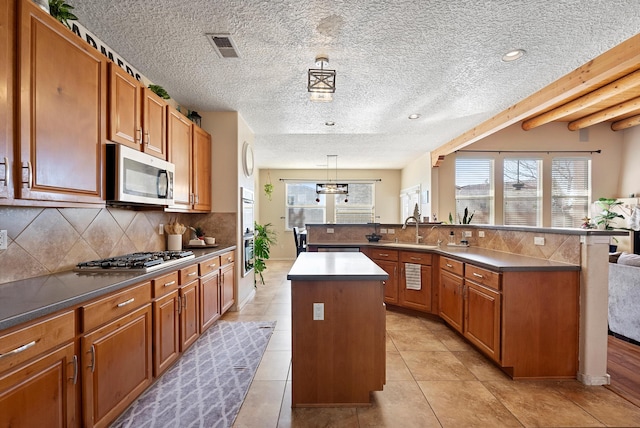 kitchen with brown cabinetry, a kitchen island, appliances with stainless steel finishes, a sink, and backsplash