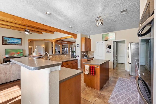 kitchen featuring open floor plan, brown cabinets, a large island with sink, and beam ceiling