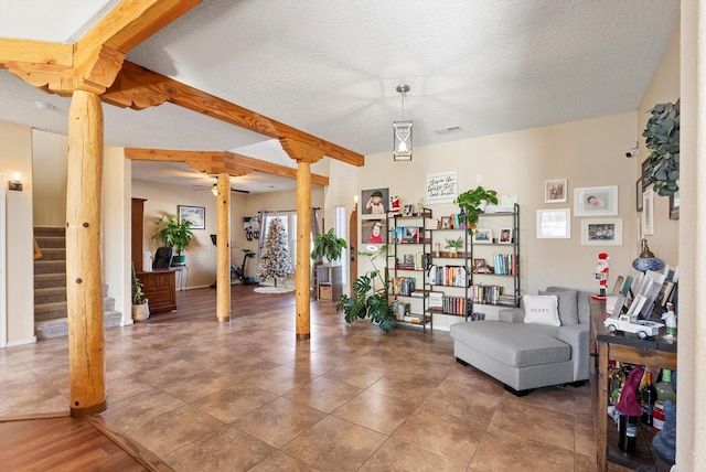 living area with beam ceiling, visible vents, a textured ceiling, ornate columns, and stairs