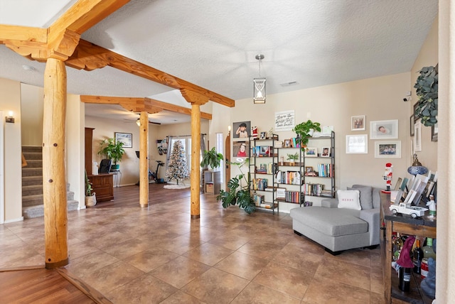 living area featuring a textured ceiling, visible vents, ornate columns, stairs, and beam ceiling