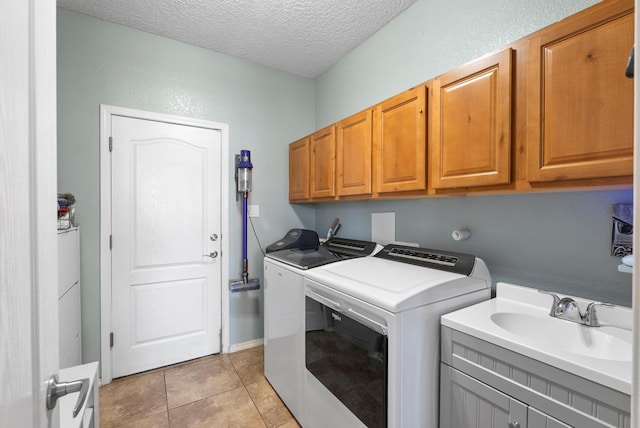 washroom featuring a textured ceiling, a sink, washer and clothes dryer, cabinet space, and light tile patterned floors