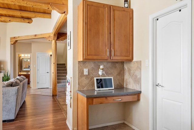 kitchen with wood finished floors, brown cabinets, tasteful backsplash, beamed ceiling, and dark countertops