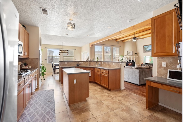 kitchen featuring a warm lit fireplace, visible vents, appliances with stainless steel finishes, open floor plan, and a center island