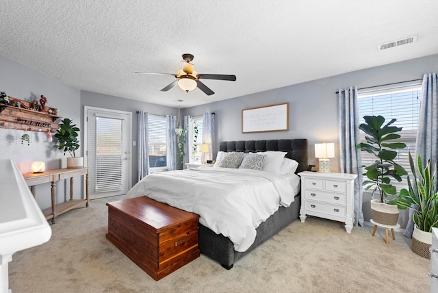 bedroom with access to exterior, light colored carpet, visible vents, ceiling fan, and a textured ceiling