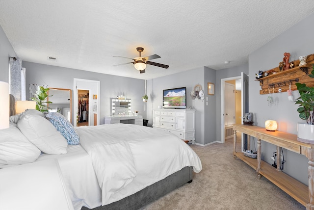 bedroom with a textured ceiling, ceiling fan, light colored carpet, visible vents, and a walk in closet